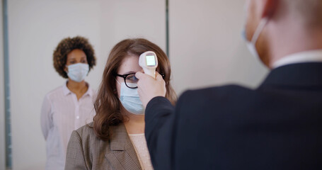 Office workers in safety mask checked with non-contact thermometer during coronavirus pandemic