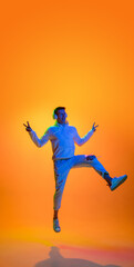 Fototapeta na wymiar Flying. Caucasian man's portrait isolated on yellow studio background in mixed neon light. Listening music in headphones. Concept of human emotions, facial expression, sales, ad, fashion. Copyspace.