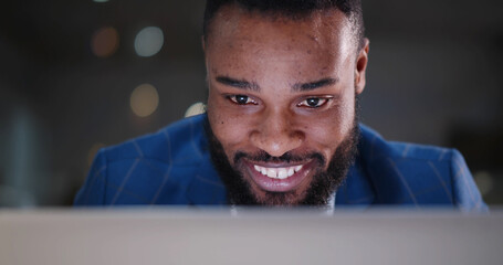 Close up of positive african businessman working on laptop in modern office.