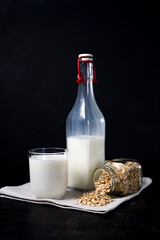 glass and bottle of vegetarian oatmeal milk on dark background