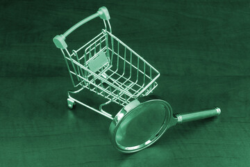 Shopping cart with magnifying glass on wooden background	