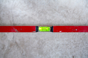 A top view of a red spirit level on a flat concrete surface.