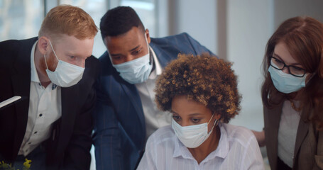 Startup team in safety mask on meeting in modern office interior brainstorming working on laptop