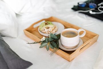 Tray with cup of coffee and light sandwich in a bed with Laptop on the background, morning light
