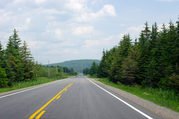 Fototapeta na wymiar straight empty road with yellow line leading to green mountain