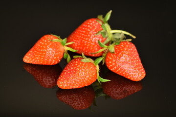 Bright red ripe strawberries with green ponytail, close-up, on a black background.