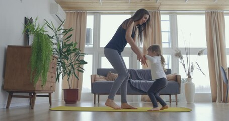 Active young mom and cute little kid daughter play on mat at living room, happy family mother with child girl having fun enjoy playing funny activity together at home