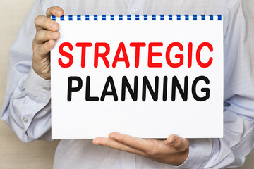 The businessman shows a sheet with the text SRATEGIC PLANNING on a white background. Business concept