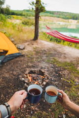 couple holding metal mugs with tea near camping fire