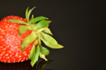 Bright red ripe strawberries with a green ponytail, close-up, on a black background.