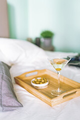Tray with martini and olives in a bed with Laptop on the background, morning light