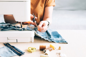 A woman tailor works at sewing machine sews reuses fabric from old denim clothes