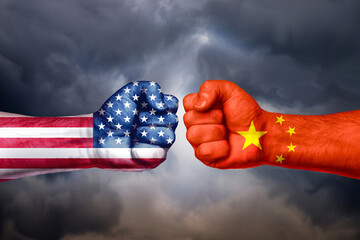 Flags of USA and China painted on two fists on sky background. United States of America versus...
