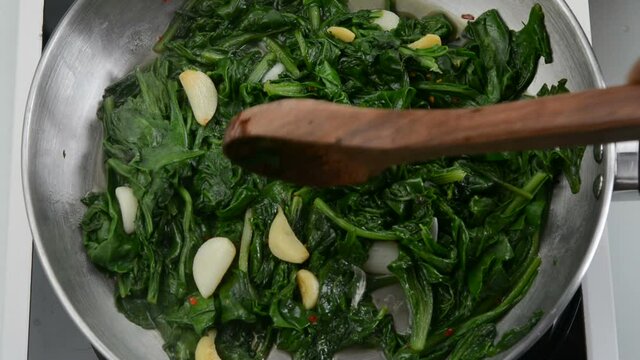 Preparing garlic sauteed spinach dish in a saucepan