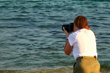  Rear view of a woman photographer taking pictures of the seascape. Selective focus. Copy space.