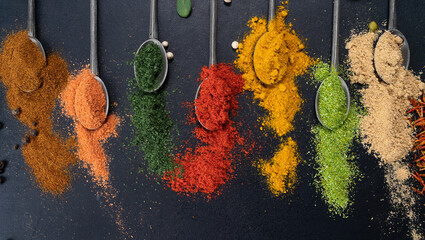 Spices and condiments in spoons for cooking on black background