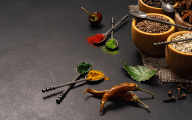 Spices and condiments in spoons and bowls for cooking on black background
