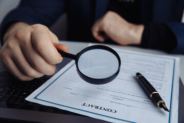Businessman looking through magnifying glass to a contract.