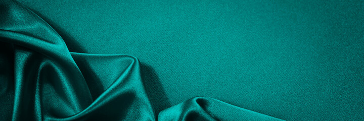 Blue green silk satin background. Soft wavy folds on smooth, shiny fabric. Dark teal luxury...