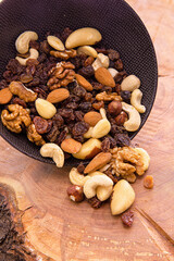 a mix of sliced dried fruits and berries, nuts spilling out of a dark cup on a wooden background