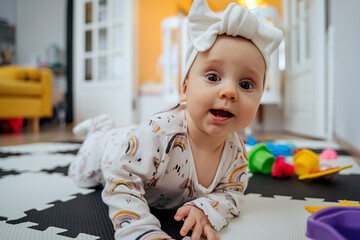 Adorable infant child  looking at camera and playing  with toys on leisure rug at home.