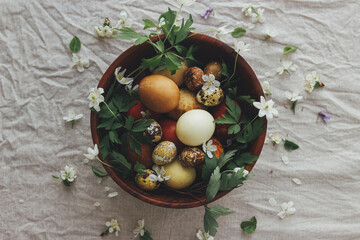 Easter eggs with spring flowers in wooden bowl on rustic linen background, top view. Aesthetic