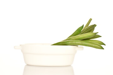 A few pods of bright green, organic, natural, ripe beans in a white ceramic plate on a white background.