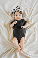 Cute baby in trendy garment and leopard headband and black bodysuit  lying on bed. Stylish  infant...
