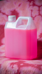 Bidón de plástico blanco con tapón de rosca blanco con lejía rosa sobre tela descolorida con...