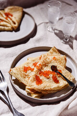 Traditional Russian crepes or pancakes with red caviar on gray plates and glasses of ice vodka over greige linen tablecloth. Pancake week or Shrovetide