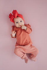 Stylish cute infant sucking finger. Adorable infant in trendy headband looking at camera while lying on floor at home