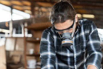 Fototapeta premium Male carpenter wearing safety goggles and dust filter mask at the carpentry workshop. Joiner working and wearing safety goggles and dust filter mask