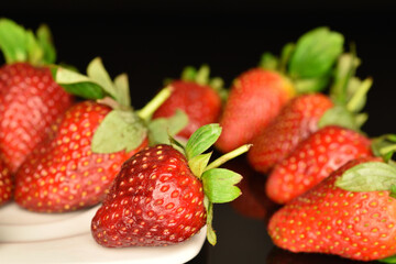 Several berries of bright red ripe organic tasty strawberries on a white ceramic saucer. The background is black.