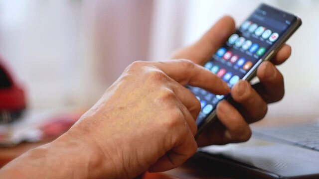 Close up of wrinkled elderly man's hand teaching smartphone use. A senior citizen uses a digital gadget close-up. Senior citizen launches app on smartphone, selective focus, shallow depth of field