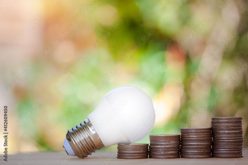 Poster led bulb on coins stack with green bokeh background with warm light to show save energy, saving mone