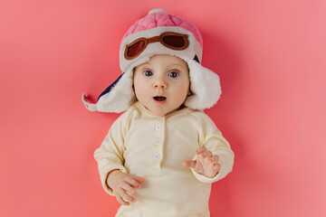 Сute infant wearing pilot hat lying on pink background  pretending being pilot