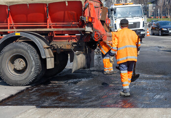 A team of road workers with a hot asphalt truck repairing a section of the road.