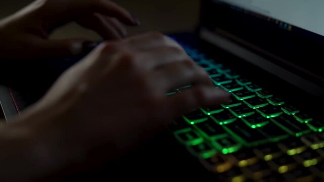 Closeup female hands is typing on laptop keyboard with colored backlight. Software developer freelancer woman work with program code on workplace at night. Programmer girl develops web application.