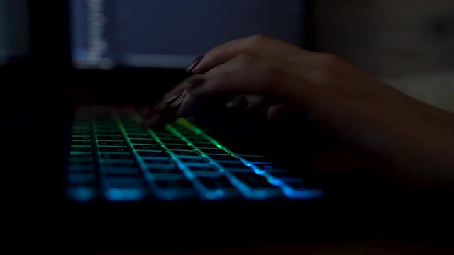 Closeup female hands is typing on laptop keyboard with colored backlight. Software developer freelancer woman work with program code on workplace at night. Programmer girl develops web application.