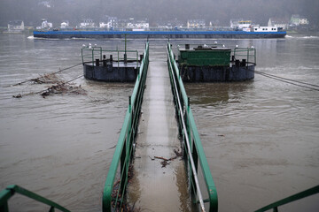 Schiffsanleger bei Hocchwasser und Binnenschiff auf dem Rhein bei Koblenz im Winter bei Regenwetter...