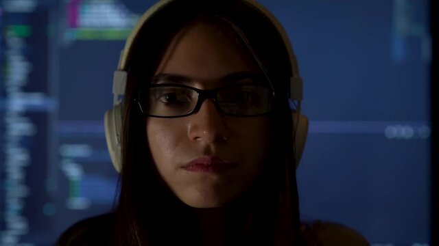 Portrait of software developer freelancer woman female in glasses work with program code on laptop at workplace at night. Programmer girl develops web desktop mobile application. Projector background.