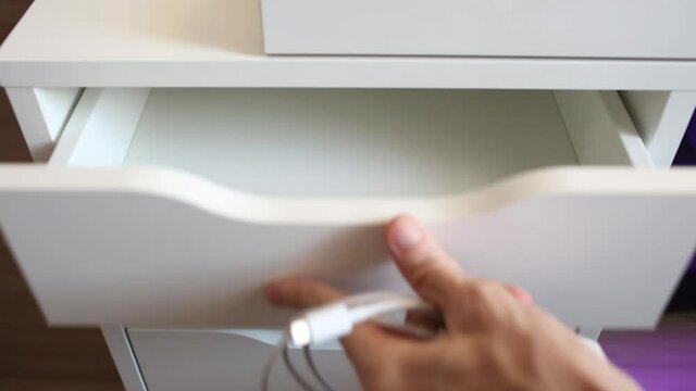 Man takes a mobile phone charger from the drawer of the nightstand. USB cable and adapter to charge your phone.