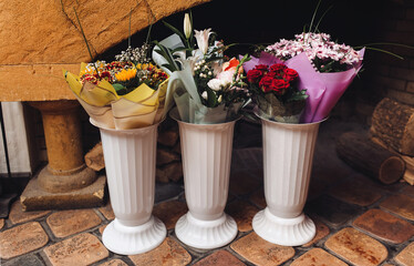 Three white vases with bouquets of flowers near the fireplace with firewood. Congratulations and gifts from guests at a wedding or birthday.