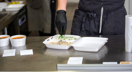 Fototapeta na wymiar Chef preparing dish to a box in the restaurant for food delivery service to home, online ordering