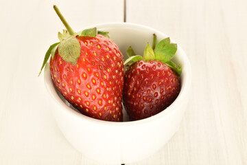 Several berries of bright red ripe organic delicious strawberries in a ceramic plate on a white wooden painted tabletop.