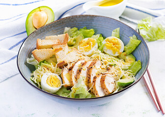 Caesar salad with lettuce, chicken, avocado and croutons on light table.