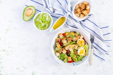 Caesar salad with lettuce, chicken, avocado, cherry tomatoes and croutons on light table. Top view, above, copy space