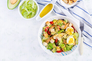 Caesar salad with lettuce, chicken, avocado, cherry tomatoes and croutons on light table. Top view, above, copy space