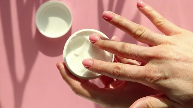 woman hand takes moisturizer cream jar close up skincare natural cosmetic on pink background sunlight effect