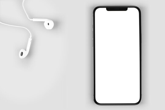 smartphone mockup iPhone 12 Pro Max with blank white screen and headphones EarPods, top view. Apple is a multinational technology company. Moscow, Russia - January 14, 2021